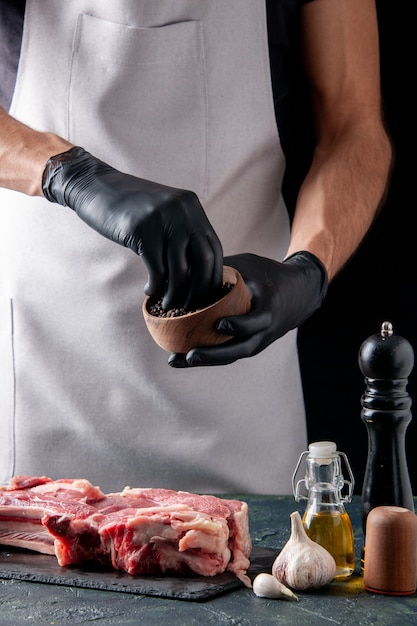 Free photo front view male butcher pouring pepper on meat slice on dark surface