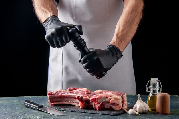 Мужчина-мясник, вид спереди, наливает перец на ломтик мяса на темной поверхности