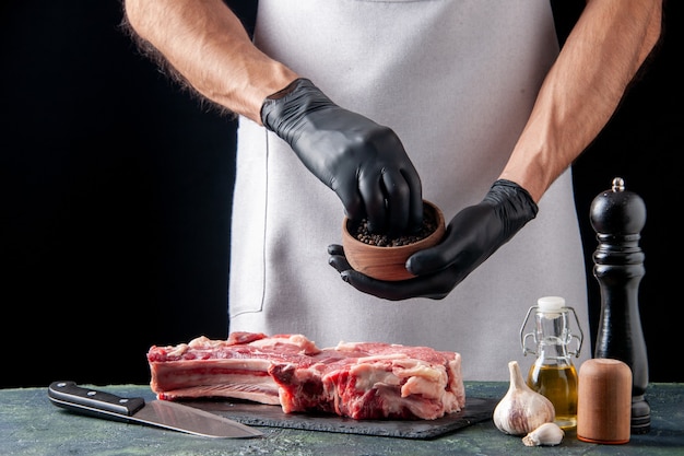 Front view male butcher pouring pepper on meat slice on dark surface