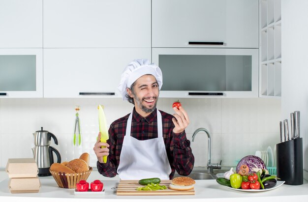 Front view male chef holding tomato and knife in the kitchen