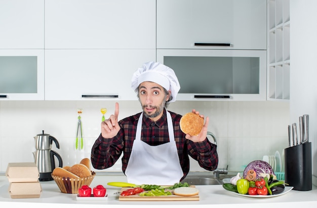 Front view male chef holding up burger bread in the kitchen