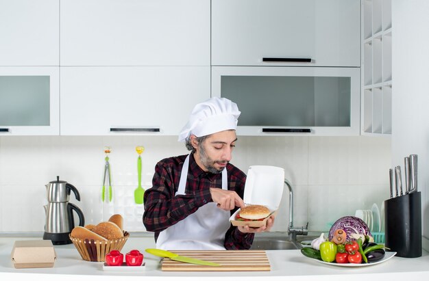 Front view male chef holding up burger in the kitchen