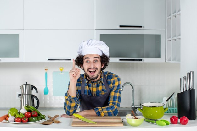 Front view of male chef with fresh vegetables pointing with happy facial expression in the white kitchen