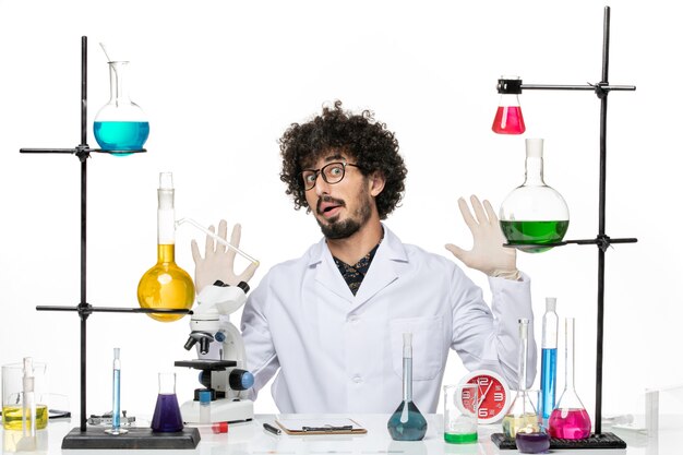 Front view male chemist in medical suit just sitting in front of table with solutions on white space