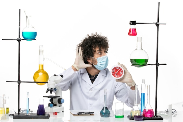 Вид спереди мужской химик в медицинском костюме и с маской, держащей часы на светлом белом пространстве