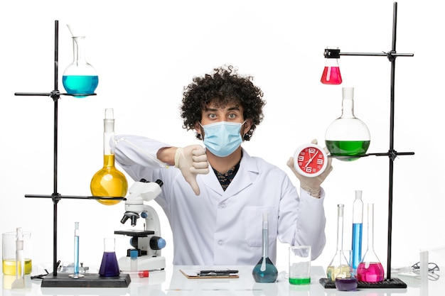 Front view male chemist in medical suit and with mask holding clock on white space