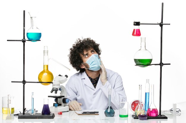 医療スーツとマスクを身に着けている正面図の男性化学者は、空白を考えてさまざまなソリューションで座っている