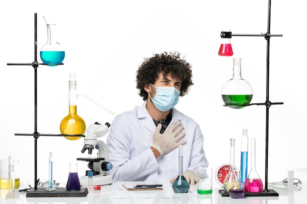 Front view male chemist in medical suit and with mask just sitting with solutions on a light white space