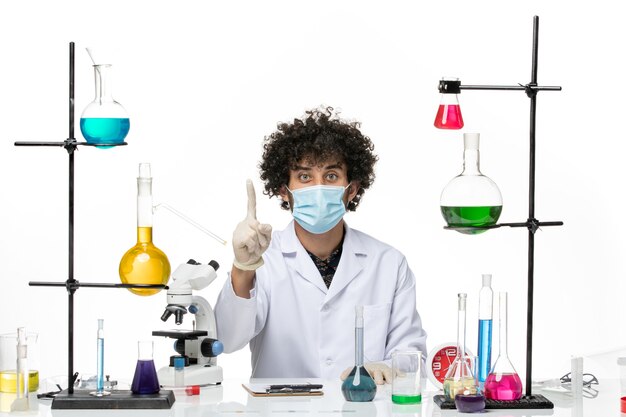 Front view male chemist in medical suit and with mask just sitting with solutions on white desk