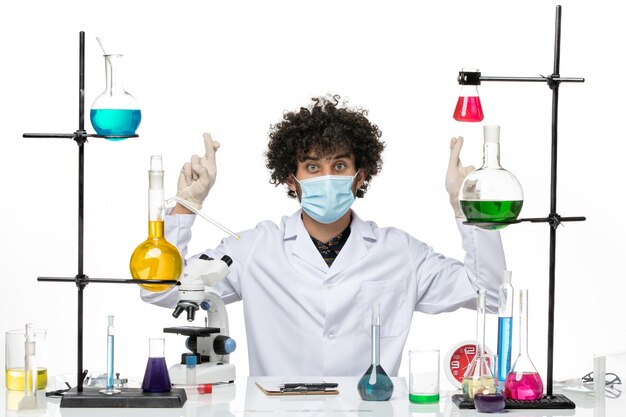 의료 소송 및 마스크가 흰색 바닥에 솔루션과 함께 앉아있는 전면보기 남성 화학자 covid- science virus male lab