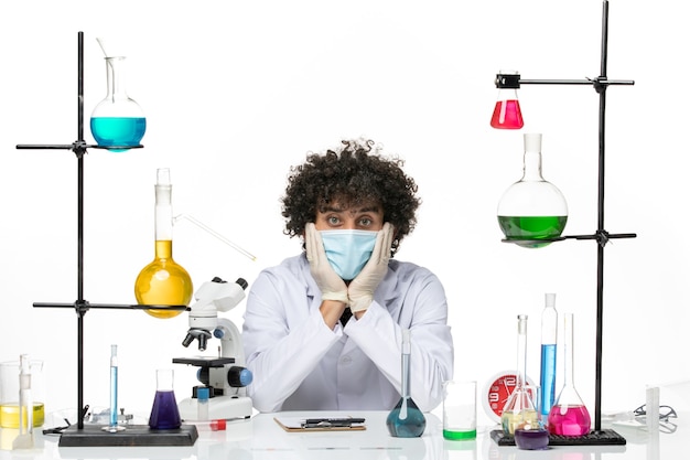 Вид спереди мужской химик в медицинском костюме и с маской, просто сидящий с растворами на белом пространстве