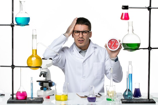 Front view male chemist in white medical suit holding clocks on the white background covid virus disease science lab