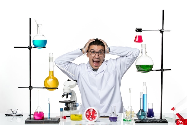 흰색 의료 소송에서 전면보기 남성 화학자 앉아서 흰색 배경에 재미있는 얼굴 만들기 바이러스 과학 covid- pandemic lab