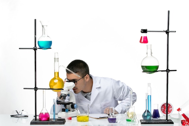 Front view male chemist in white medical suit using microscope on a white background virus covid- disease science