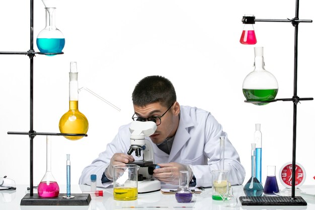 白い背景に顕微鏡を使用して白い医療スーツを着た男性化学者の正面図ウイルス研究所