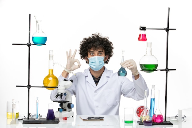 Front view male chemist in white medical suit and with mask holding blue solution on light white space