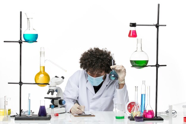 Front view male chemist in white medical suit and with mask holding solution writing on a white space