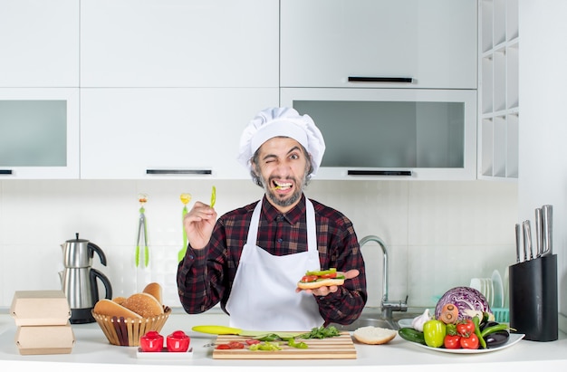 Vista frontale del cuoco maschio che aggiunge pepe all'hamburger in piedi dietro il tavolo della cucina