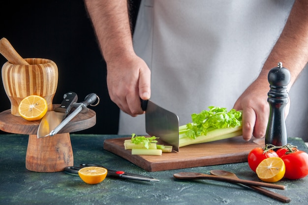 Front view male cook cutting celery on a dark wall salad diet meal color photo food health