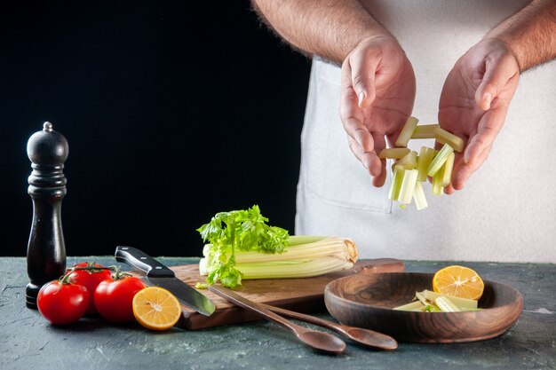 Вид спереди мужчина повар резка сельдерея на темной стене салат диетическая еда фото пищевые красители готовка кухня