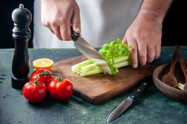 Вид спереди мужской повар, режущий сельдерей на темной стене, салат, диета, еда, фото, еда, здоровье, цвета