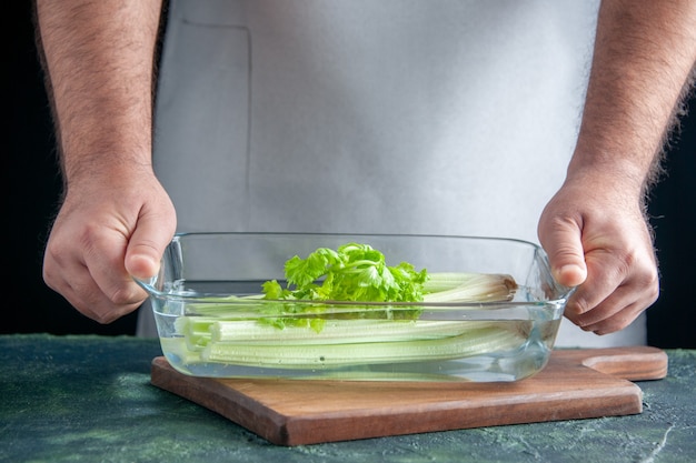 Front view male cook holding plate with celery on dark wall salad diet meal color photo food health