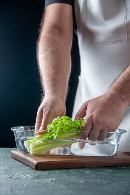 Вид спереди мужчина-повар вынимает сельдерей из тарелки с водой на темной стене салат диета еда цвет фото еда здоровье