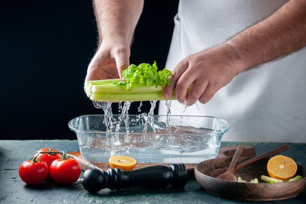 Вид спереди мужчина-повар вынимает сельдерей из тарелки с водой на темной стене салат диетическое питание фото еда здоровье цвет