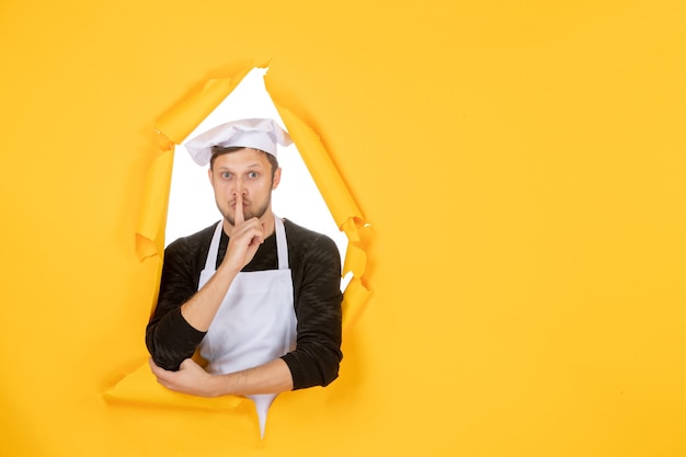 Front view male cook in white cape and cap on yellow ripped cuisine color job kitchen food man