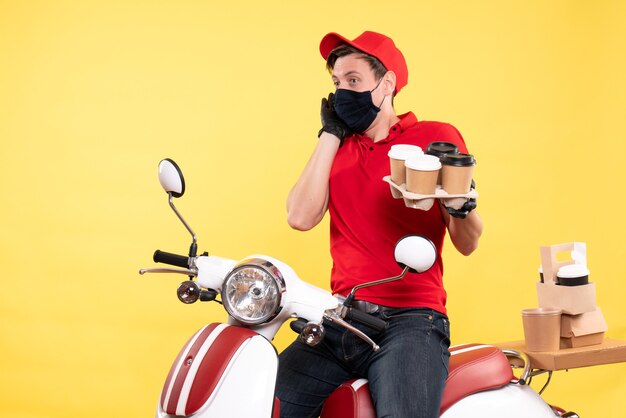 Front view male courier on bike in mask with coffee on yellow 