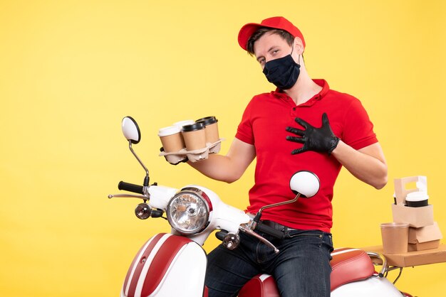 Front view male courier on bike in mask with coffee on yellow 