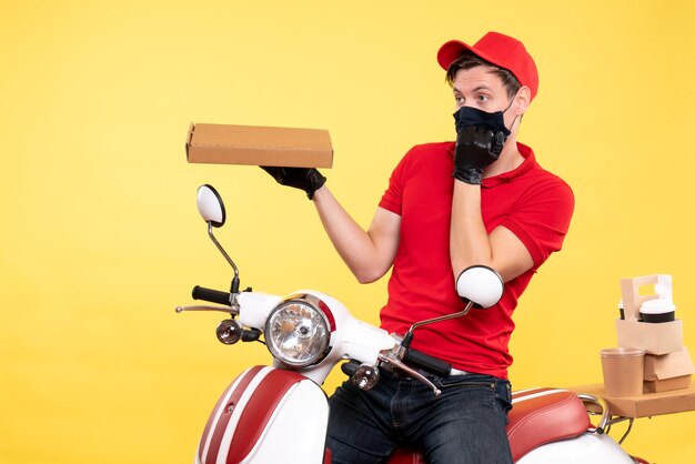 Front view male courier on bike in mask with food box on yellow 