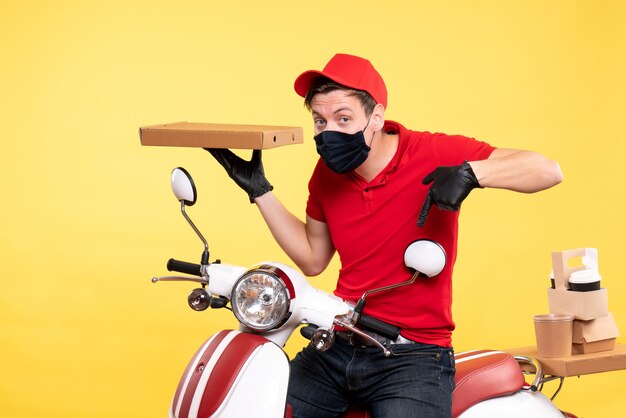 Front view male courier on bike in mask with food box on yellow 