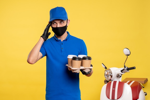 黄色い仕事でコーヒーを保持している黒いマスクの正面図男性宅配便パンデミックサービス提供均一な仕事