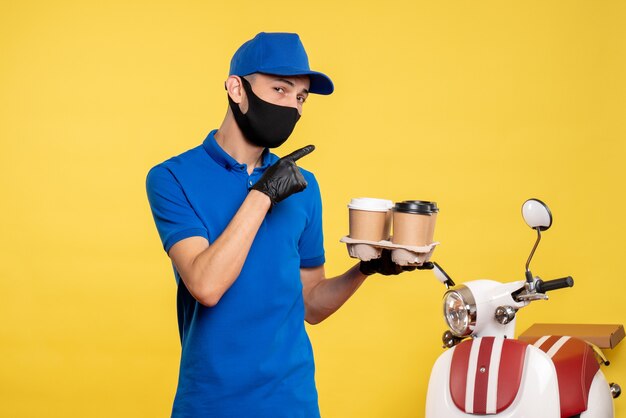 黄色い仕事でコーヒーを保持している黒いマスクの正面図男性宅配便パンデミックサービス提供均一な仕事