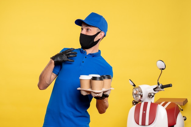 Free photo front view male courier in black mask holding coffee on yellow pandemic delivery job covid- service uniform work