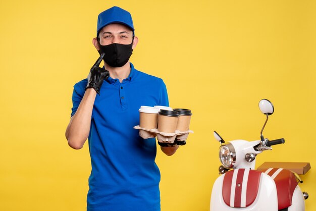 Front view male courier in black mask holding coffee on yellow work delivery job covid pandemic service