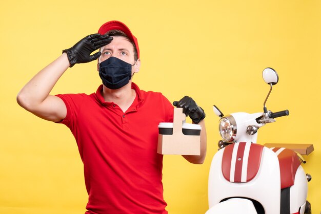 Front view male courier in black mask with coffee cups on a yellow job virus covid- delivery worker uniform work service