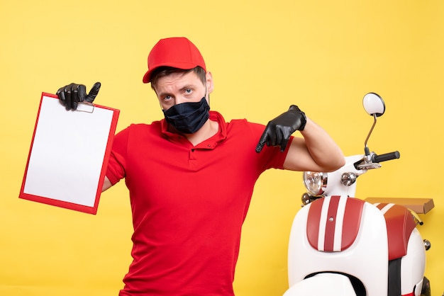 Front view male courier in black mask with file note on yellow uniform covid delivery pandemic work service virus