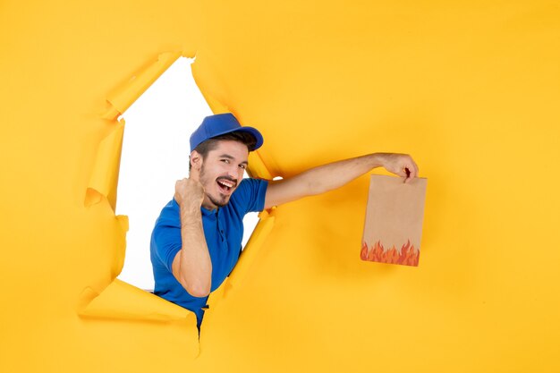 Курьер-мужчина, вид спереди в синей форме, дающий пакет с едой на желтом пространстве