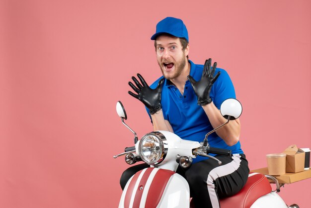 Front view male courier in blue uniform and gloves on pink color work fast-food bike service food job delivery