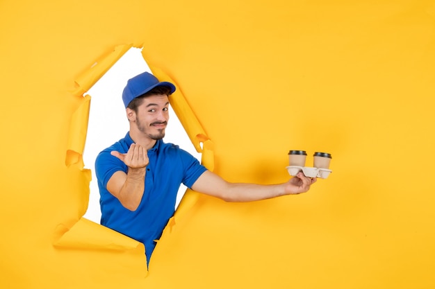 Front view male courier in blue uniform holding coffee cups on the yellow space