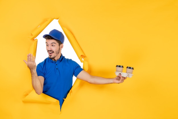 Front view male courier in blue uniform holding coffee cups on yellow space