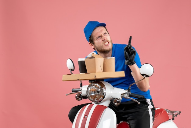 Front view male courier in blue uniform holding coffee and food box on pink fast-food work delivery job bike color service