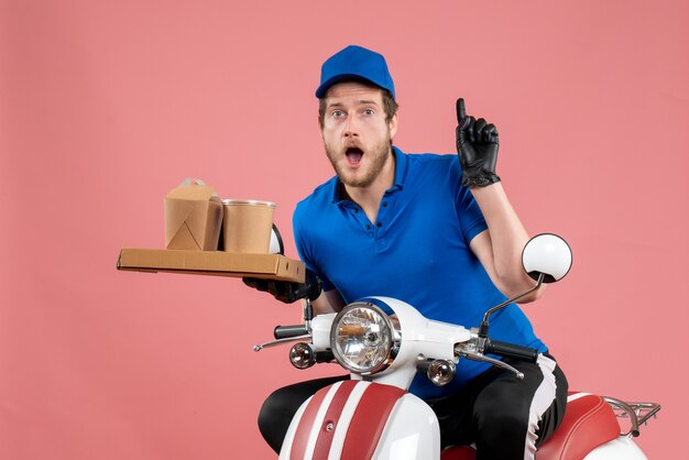 Front view male courier in blue uniform holding coffee and food box on pink fast-food work job bike color service