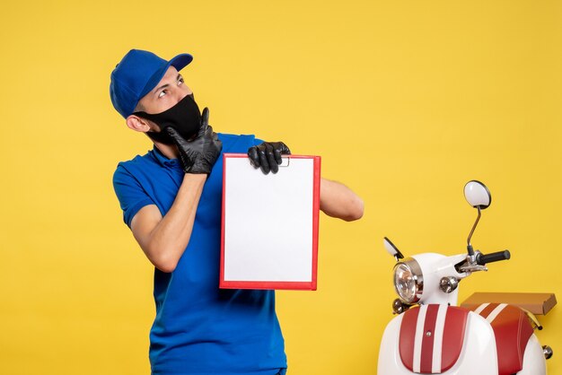Front view male courier in blue uniform holding file note on the yellow job service covid- delivery pandemic color uniform work