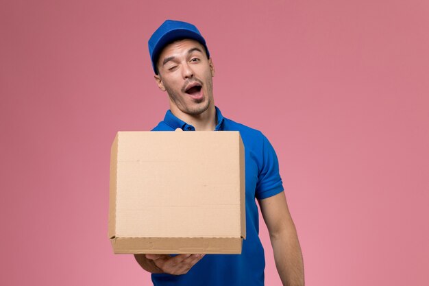 분홍색 벽, 균일 한 서비스 작업 배달에 윙크하는 음식 상자를 들고 파란색 유니폼에 전면보기 남성 택배