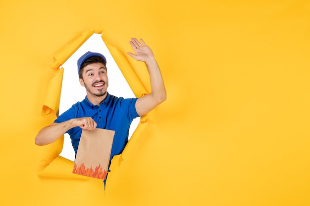 Free photo front view male courier in blue uniform holding food package on a yellow space