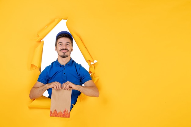 Front view male courier in blue uniform holding food package on yellow space