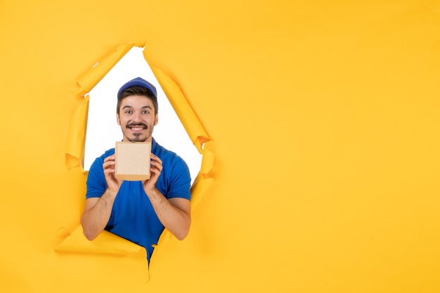 Front view male courier in blue uniform holding little food package on yellow space